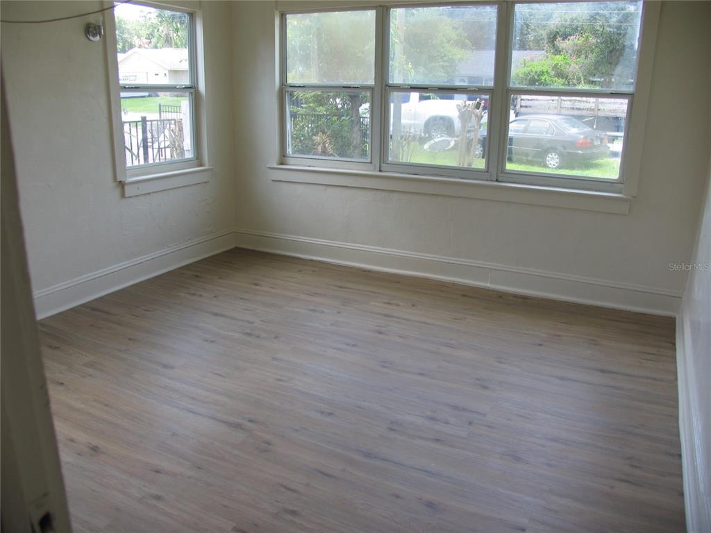 An empty room features light wood-look flooring, white walls, and multiple windows — 323 DOVER STREET, ORLANDO, FL