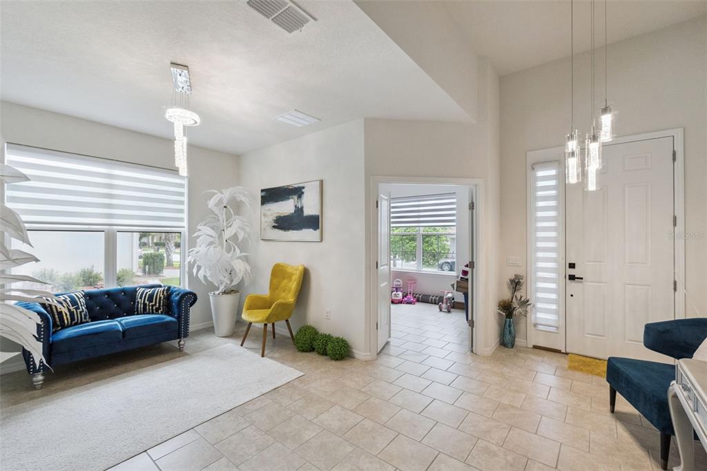 A bright foyer features tile flooring, a blue tufted sofa, a yellow chair, and pendant lighting — 3849 CARRICK BEND DRIVE, KISSIMMEE, FL