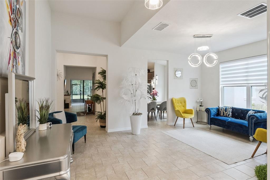 A bright living room features tiled floors, a blue sofa, yellow chairs, and modern lighting — 3849 CARRICK BEND DRIVE, KISSIMMEE, FL