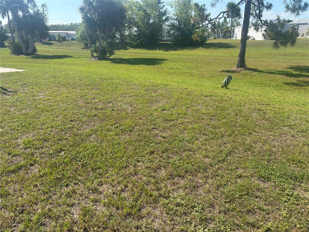 A grassy, open lot features scattered trees and distant manufactured homes under a clear sky — 7381 CANDACE LANE, PORT CHARLOTTE, FL