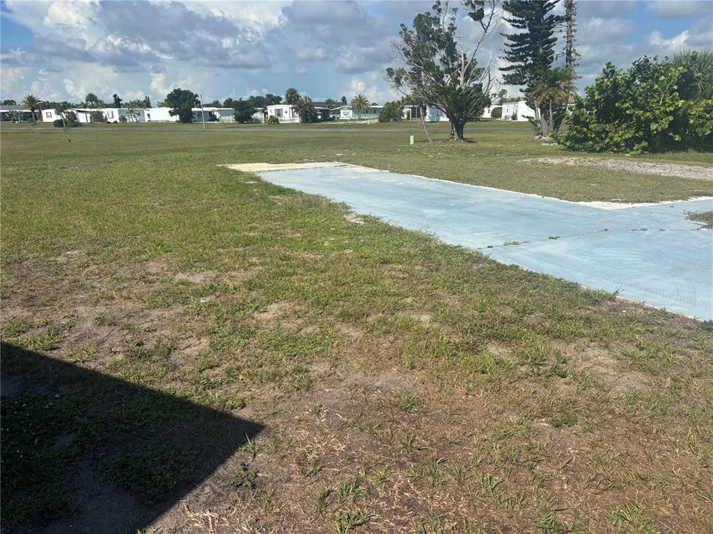A concrete slab sits in a grassy lot with distant mobile homes in the background — 7381 CANDACE LANE, PORT CHARLOTTE, FL
