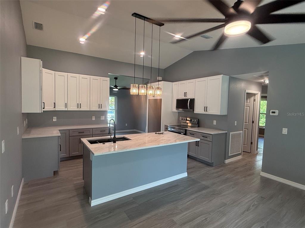 A modern kitchen features white upper cabinets, gray lower cabinets, and a central island — 2190 PENGUIN LANE, NORTH PORT, FL