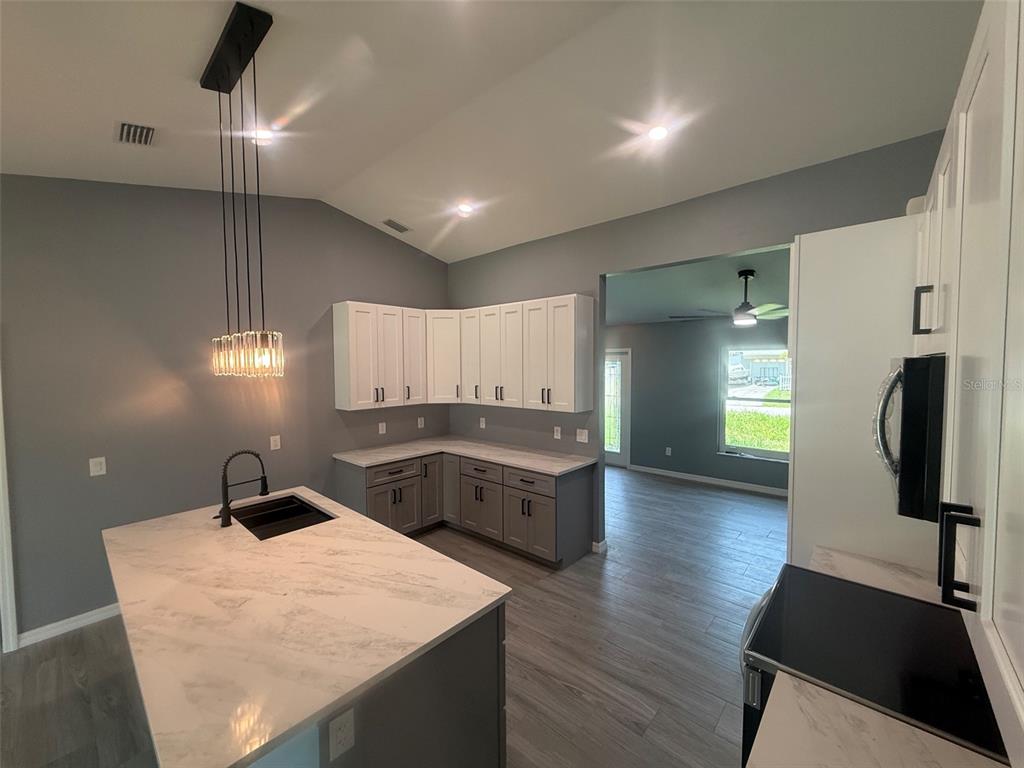 A kitchen features a marble-topped island, two-toned cabinetry, and gray flooring — 2190 PENGUIN LANE, NORTH PORT, FL