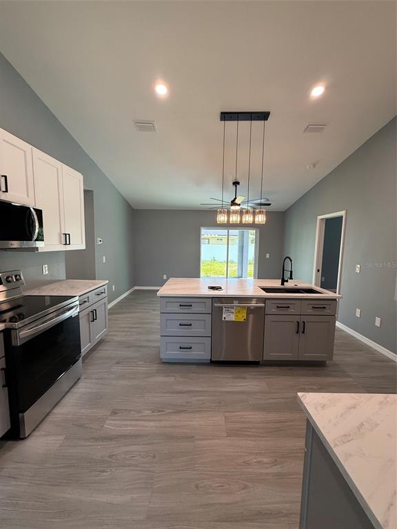 A kitchen features gray cabinets, a central island with a dishwasher, and light wood flooring — 2190 PENGUIN LANE, NORTH PORT, FL