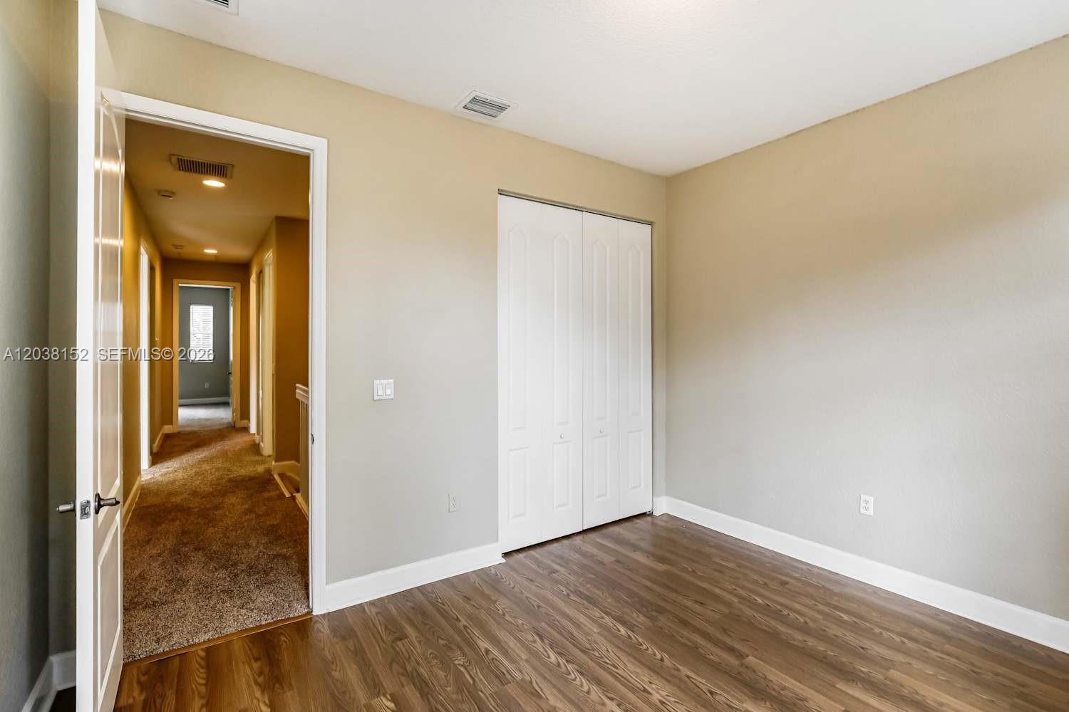 A room with wood-look flooring, beige walls, and a white bi-fold closet door — DAVIE, FL