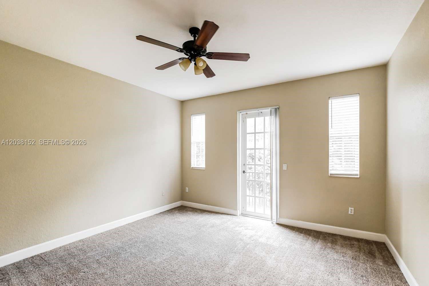 A bedroom features beige walls, gray carpeting, a ceiling fan, and a glass-paned door — DAVIE, FL