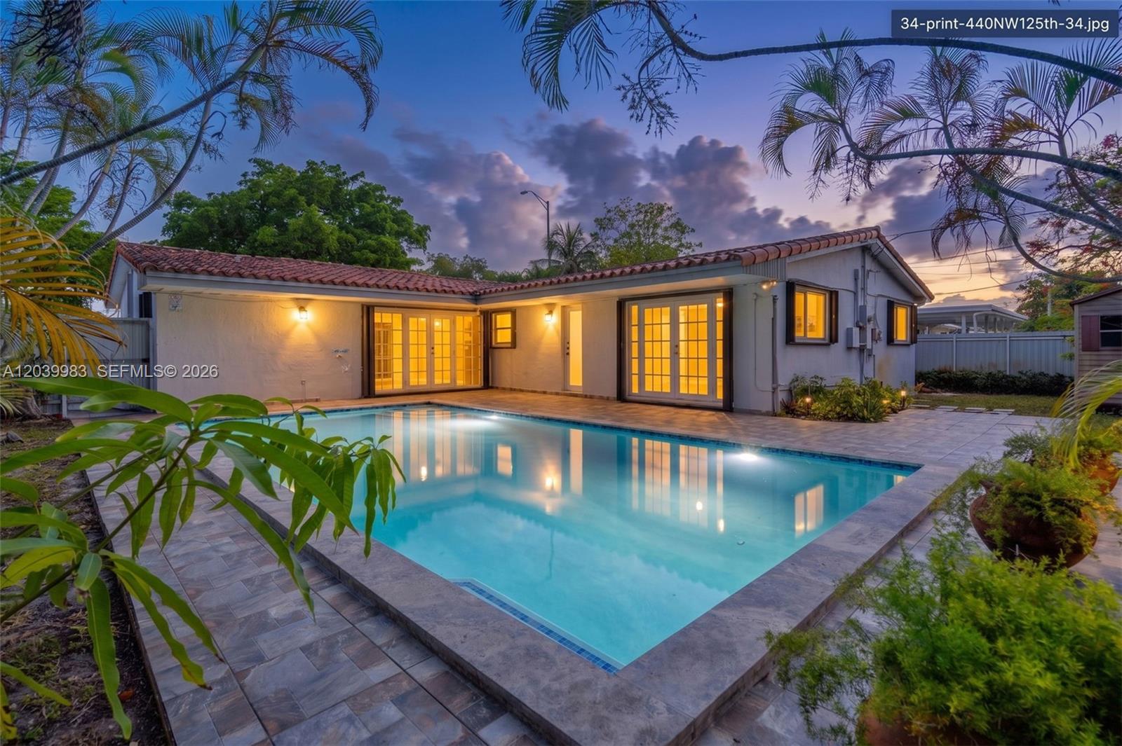 A backyard swimming pool sits on a tiled patio next to a single-story house — 440 NW 125th St, North Miami FL 33168, NORTH MIAMI, FL