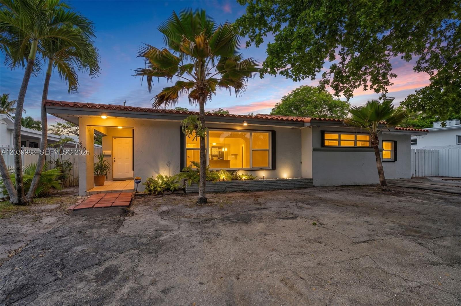 A single-story house with a flat roof, palm trees, and a paved driveway at dusk — 440 NW 125th St, North Miami FL 33168, NORTH MIAMI, FL