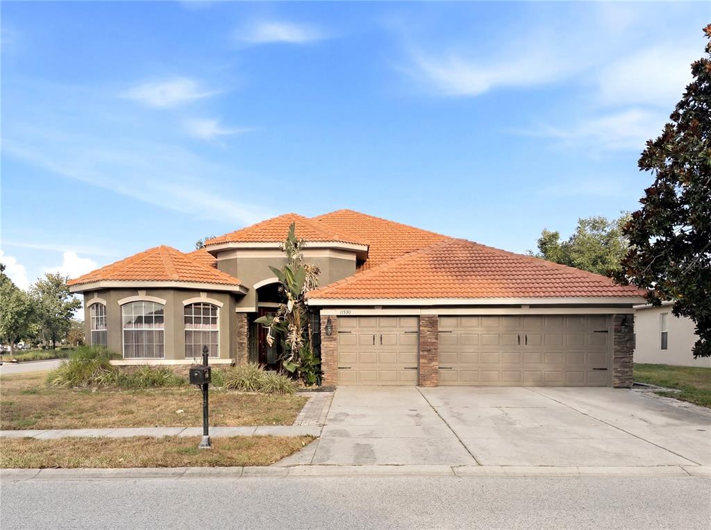 A single-story house with a terracotta tile roof, beige stucco walls, and a two-car garage — 11530 OYSTER BAY CIRCLE, NEW PORT RICHEY, FL