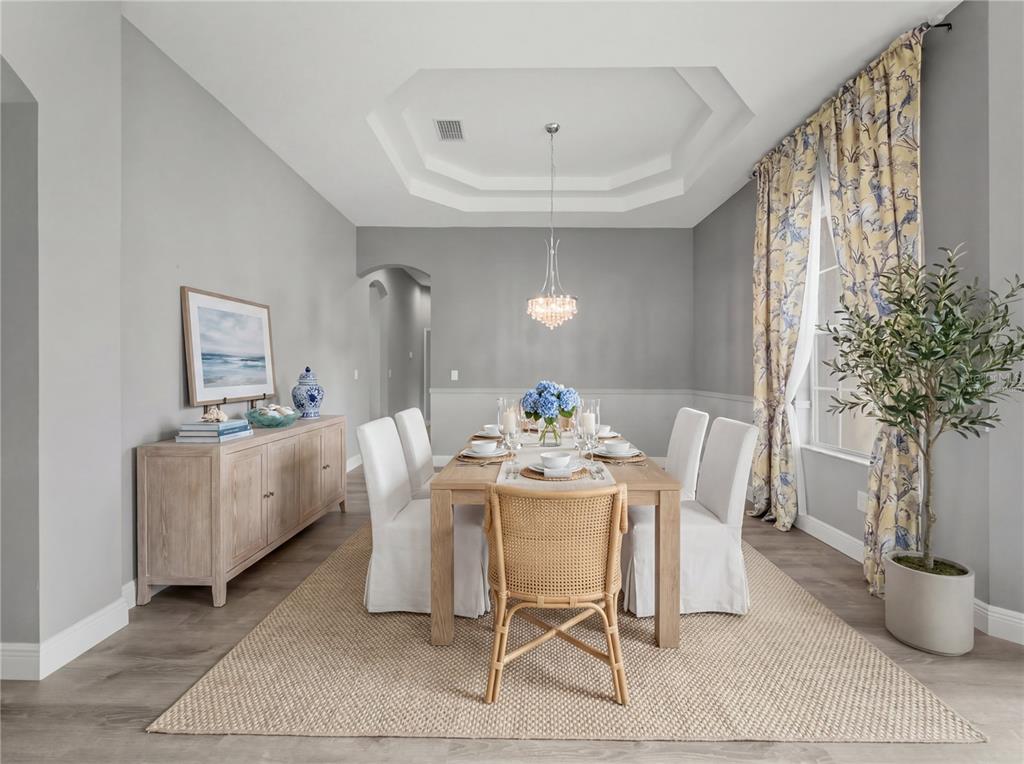 A dining room features a wooden table, white slipcovered chairs, a rattan chair, and a chandelier — 11530 OYSTER BAY CIRCLE, NEW PORT RICHEY, FL