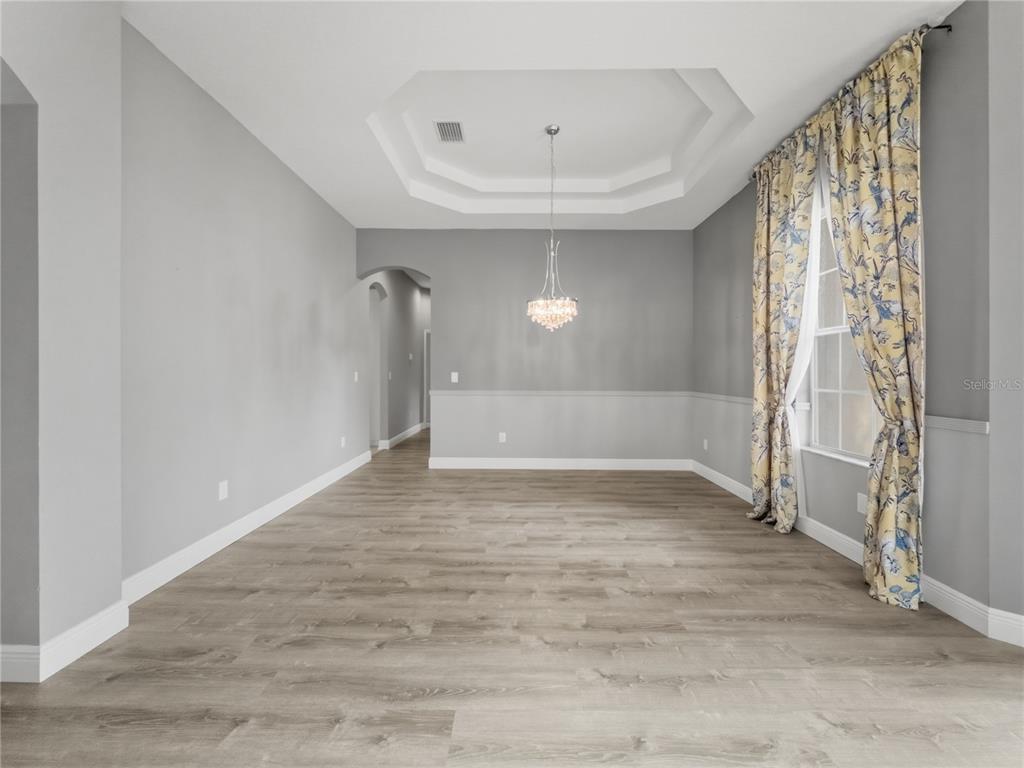 An empty dining room features gray walls, a tray ceiling, a chandelier, and wood flooring — 11530 OYSTER BAY CIRCLE, NEW PORT RICHEY, FL