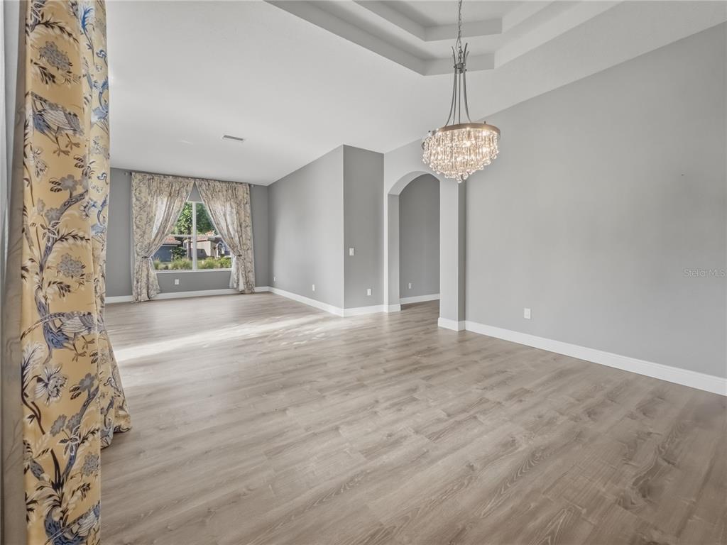 An empty room with light wood-look flooring, gray walls, a crystal chandelier, and arched entryway — 11530 OYSTER BAY CIRCLE, NEW PORT RICHEY, FL