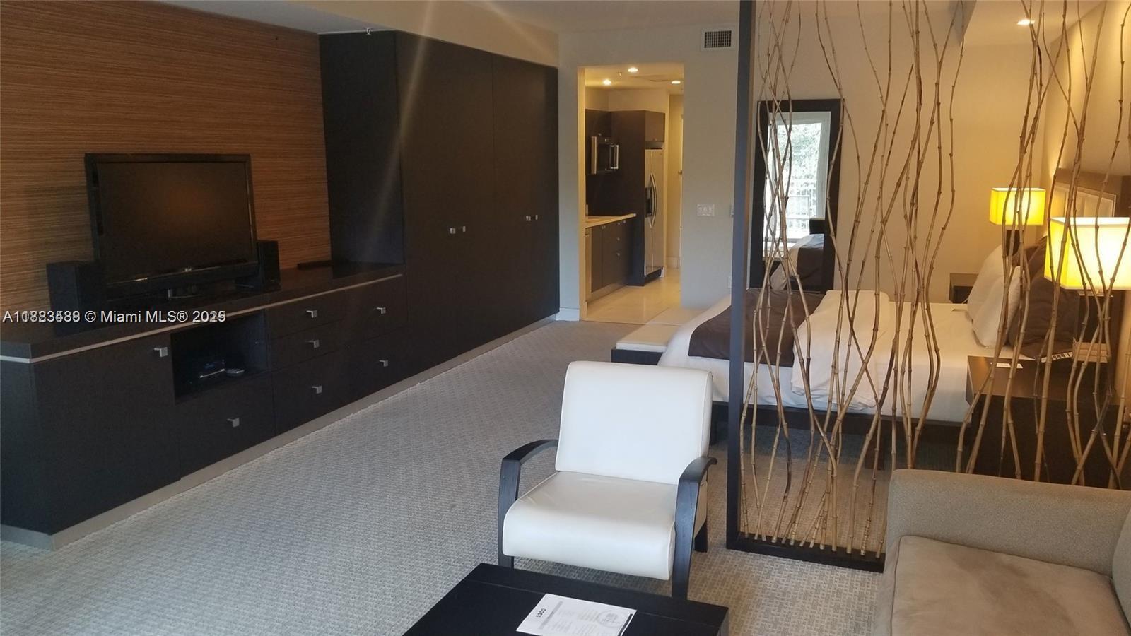 A modern studio apartment features a bed, a white armchair, and dark cabinetry — 5300 NW 87th Ave # 415, Doral FL 33178, DORAL, FL