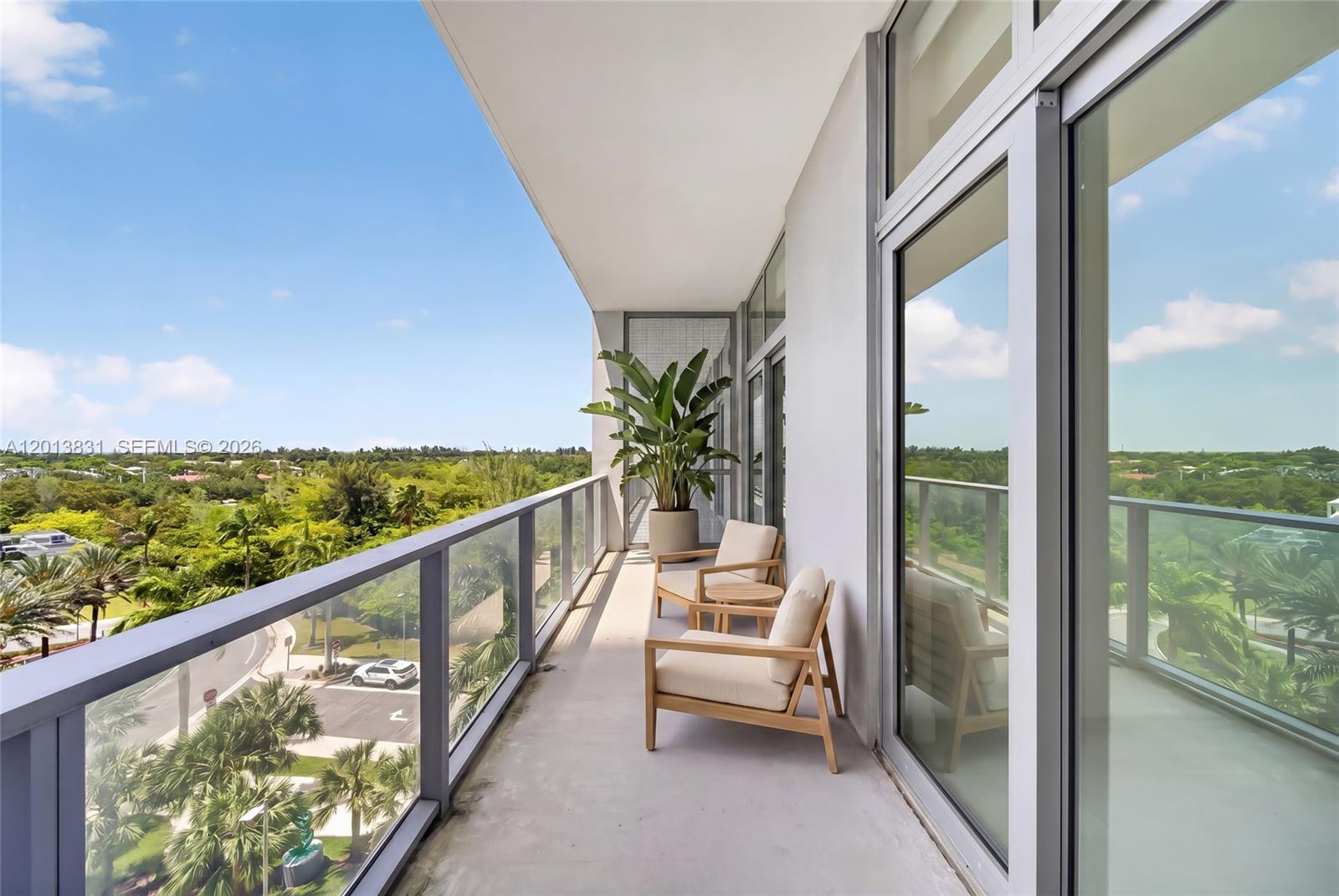 A balcony features two wooden chairs, a small table, a potted plant, and glass railings — 2000 Metropica Way # 615, Sunrise FL 33323, SUNRISE, FL