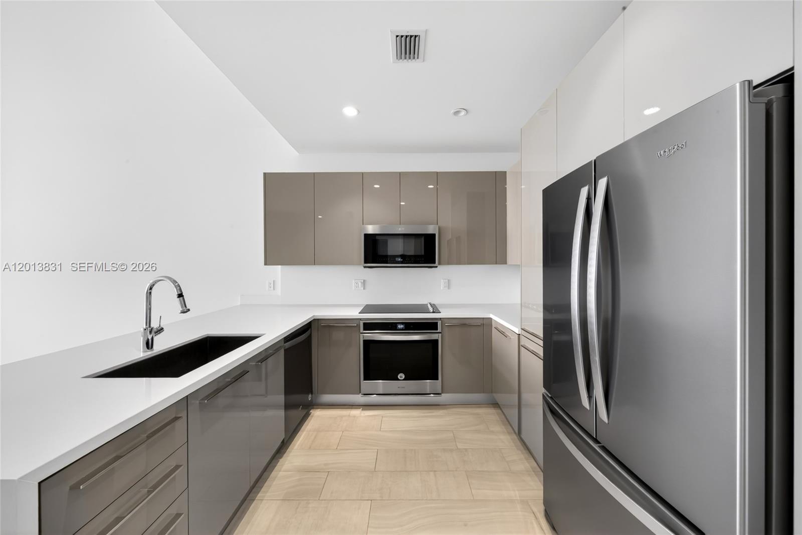 A modern kitchen features glossy taupe cabinets, stainless steel appliances, and white countertops — 2000 Metropica Way # 615, Sunrise FL 33323, SUNRISE, FL