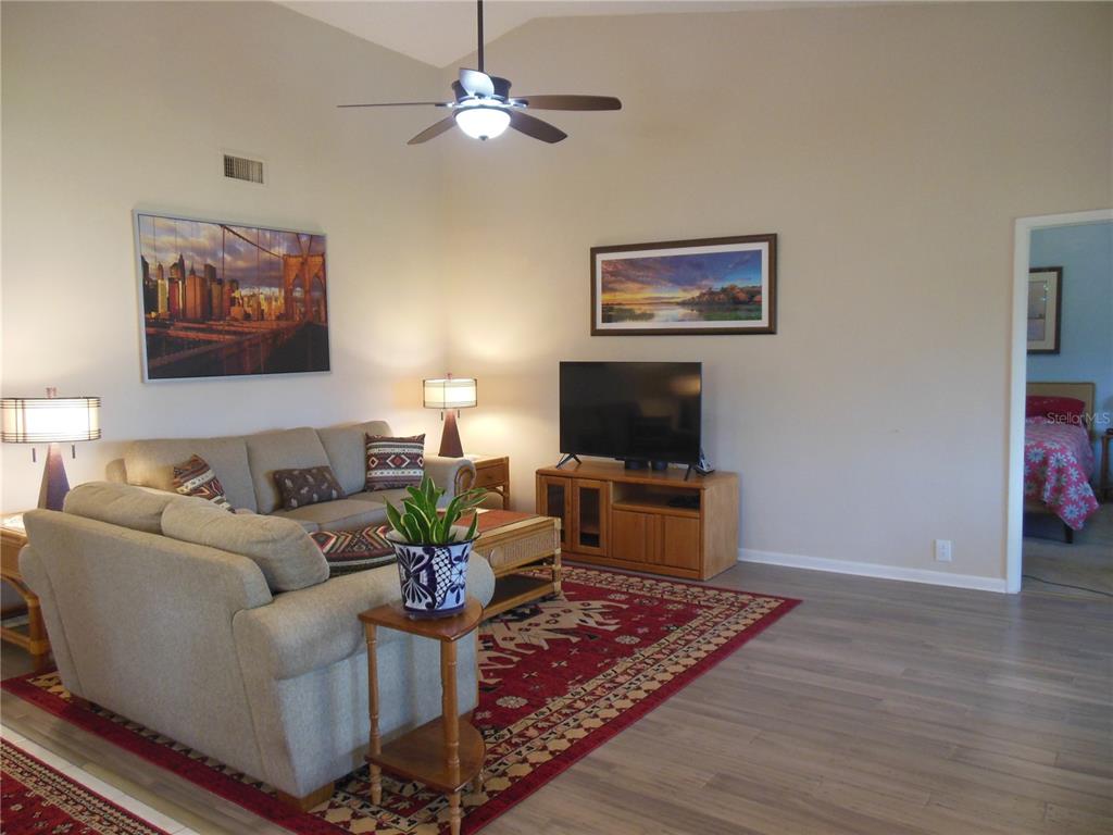 A living room features a beige sofa, a red patterned rug, and a television console — 3053 LANDMARK BOULEVARD UNIT 1107, PALM HARBOR, FL