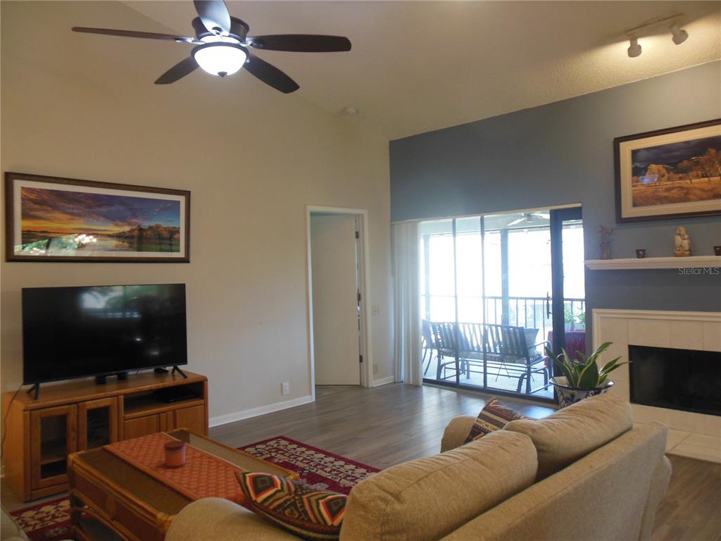 A living room features a vaulted ceiling, a fireplace, and sliding glass doors to a patio — 3053 LANDMARK BOULEVARD UNIT 1107, PALM HARBOR, FL