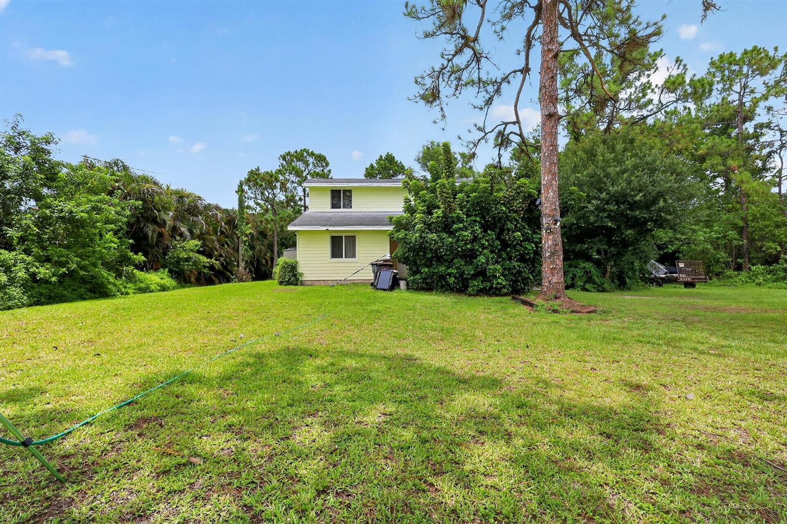 A two-story yellow house sits in a large, grassy backyard surrounded by mature trees — 16393 E Mayfair Drive E, FL 33470, FL