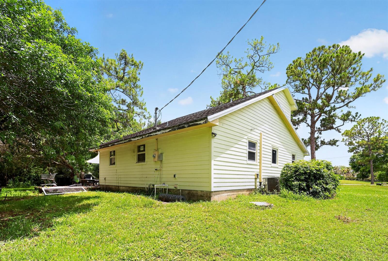 A side view of a yellow, single-story house with horizontal siding and a shingled roof — 16393 E Mayfair Drive E, FL 33470, FL
