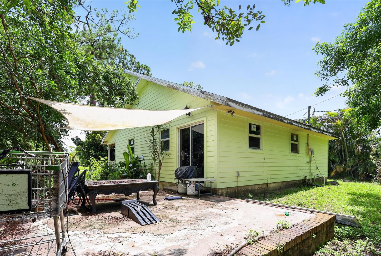 A light green house exterior features a concrete patio, a shade sail, and a shopping cart — 16393 E Mayfair Drive E, FL 33470, FL