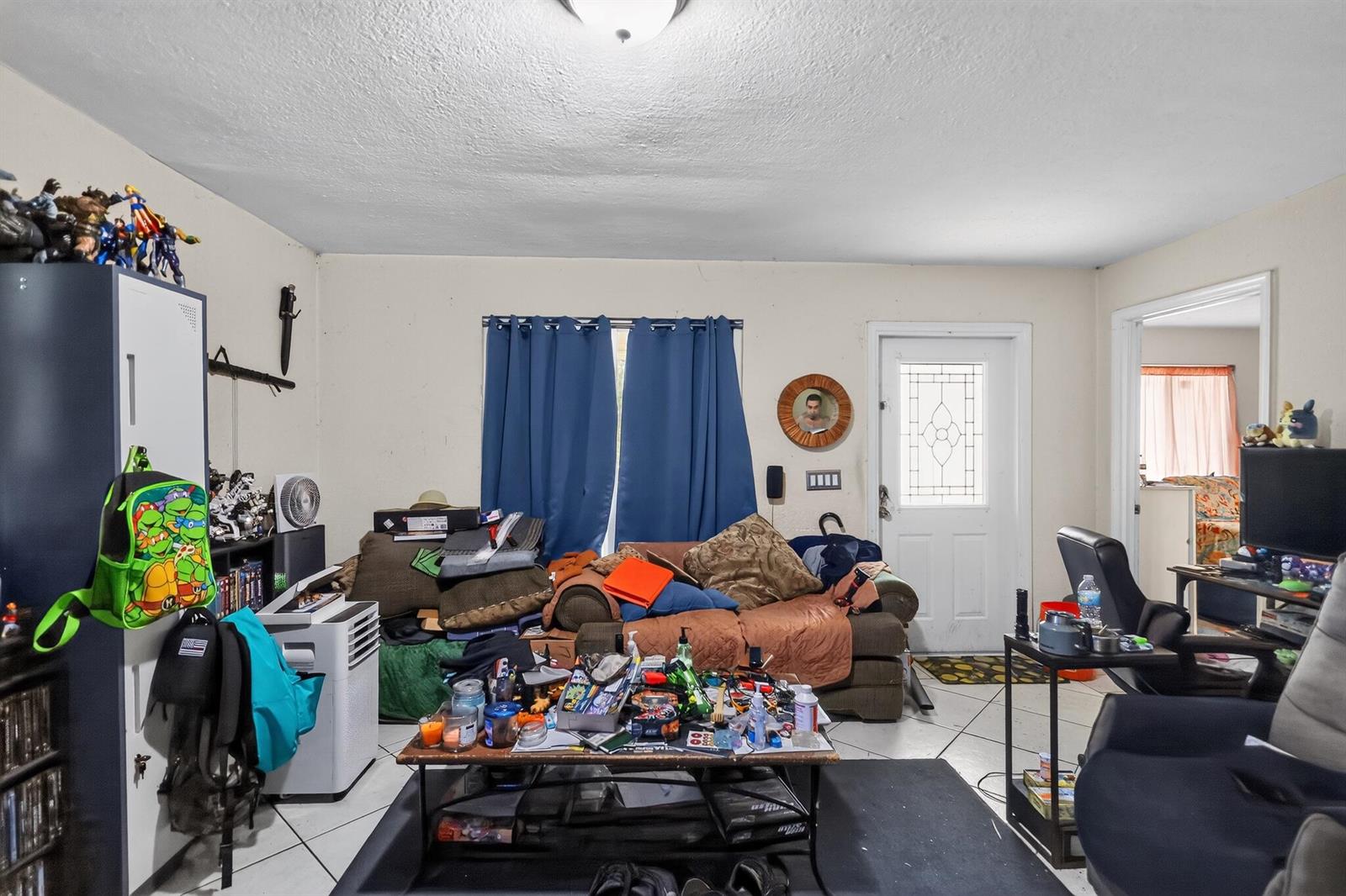 A cluttered living room features a brown sofa, a coffee table, and a white door — 16393 E Mayfair Drive E, FL 33470, FL