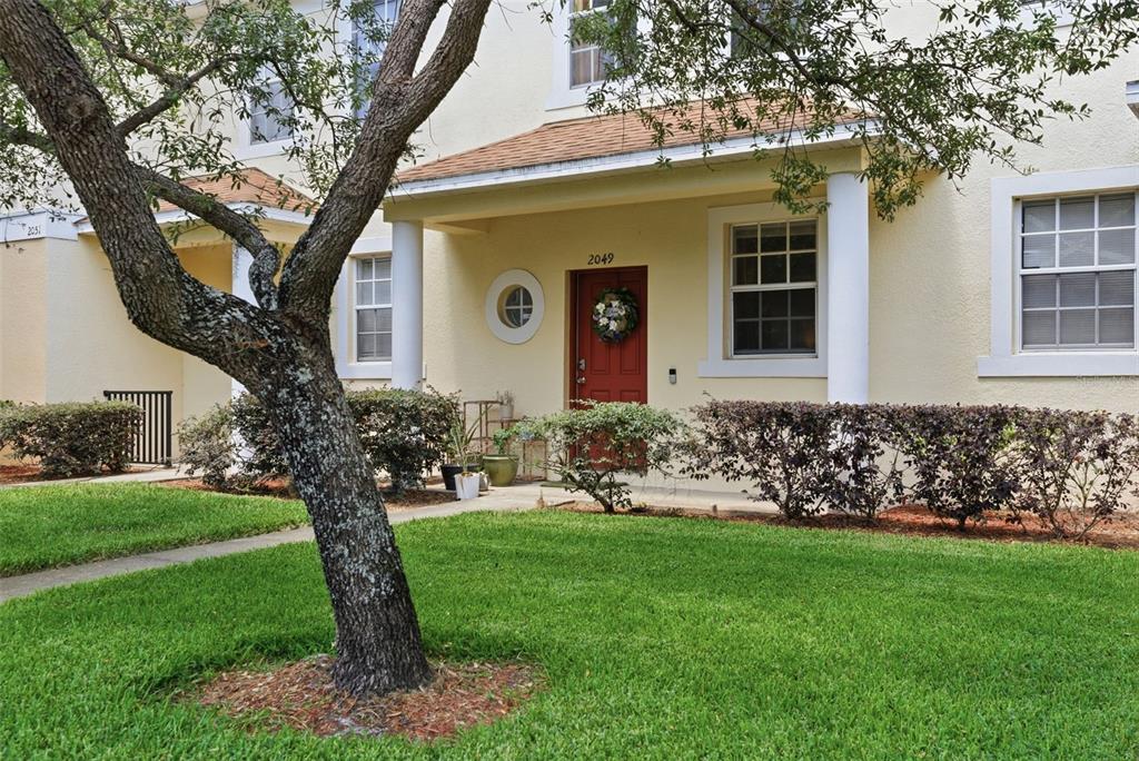 A tan two-story townhouse features a red front door, white columns, and a front lawn — 2049 FIESTA RIDGE COURT, TAMPA, FL
