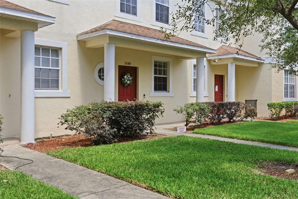 A two-story townhouse exterior with a red front door, a porch, and a front lawn — 2049 FIESTA RIDGE COURT, TAMPA, FL