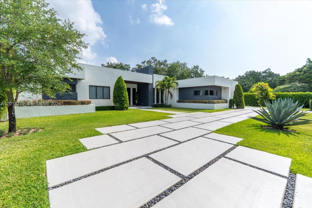 A modern, flat-roofed white house features a geometric concrete paver walkway and manicured lawn — 6785 SW 99th Ter, Pinecrest FL 33156, PINECREST, FL