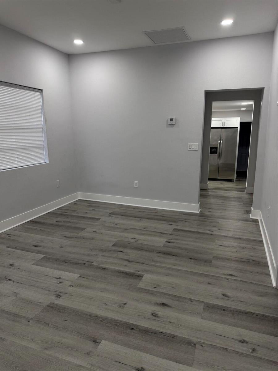 A room with gray walls, white trim, and wood-look flooring leads into a kitchen — 210 Basilan Crescent, Clewiston FL 33440, CLEWISTON, FL