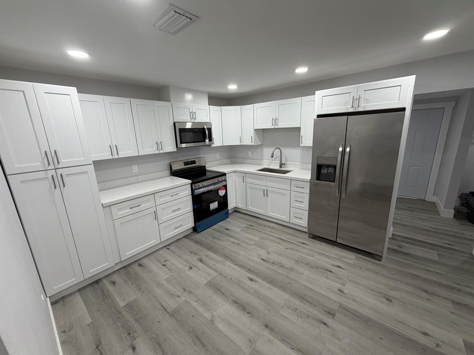 A modern kitchen features white shaker cabinets, stainless steel appliances, and light wood-look flooring — 210 Basilan Crescent, Clewiston FL 33440, CLEWISTON, FL
