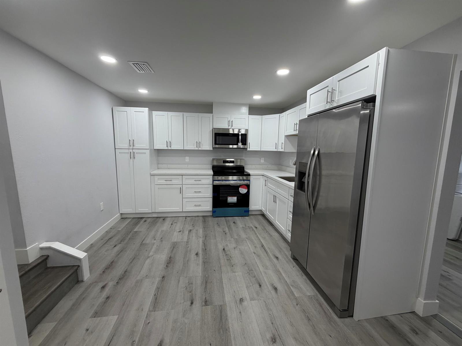 A modern kitchen features white cabinetry, stainless steel appliances, and gray wood-look flooring — 210 Basilan Crescent, Clewiston FL 33440, CLEWISTON, FL