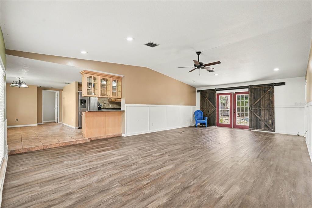 A spacious living room features wood-look flooring, white wainscoting, a vaulted ceiling, and sliding barn doors — 805 W COLLEGE AVENUE, RUSKIN, FL