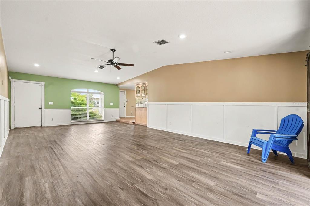 A spacious room features wood-look flooring, white wainscoting, a ceiling fan, and a blue chair — 805 W COLLEGE AVENUE, RUSKIN, FL