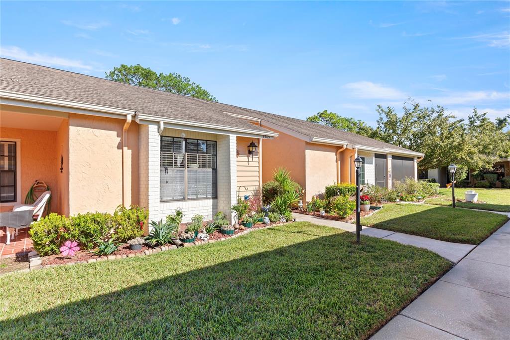 A single-story peach-colored house with a front lawn, sidewalk, and a small garden bed — 9309 TROWBRIDGE COURT, NEW PORT RICHEY, FL