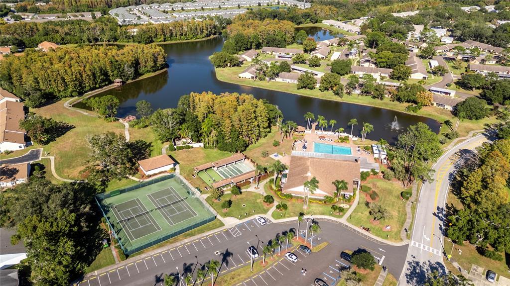 An aerial view shows a community center with a pool, tennis courts, and a lake — 9309 TROWBRIDGE COURT, NEW PORT RICHEY, FL
