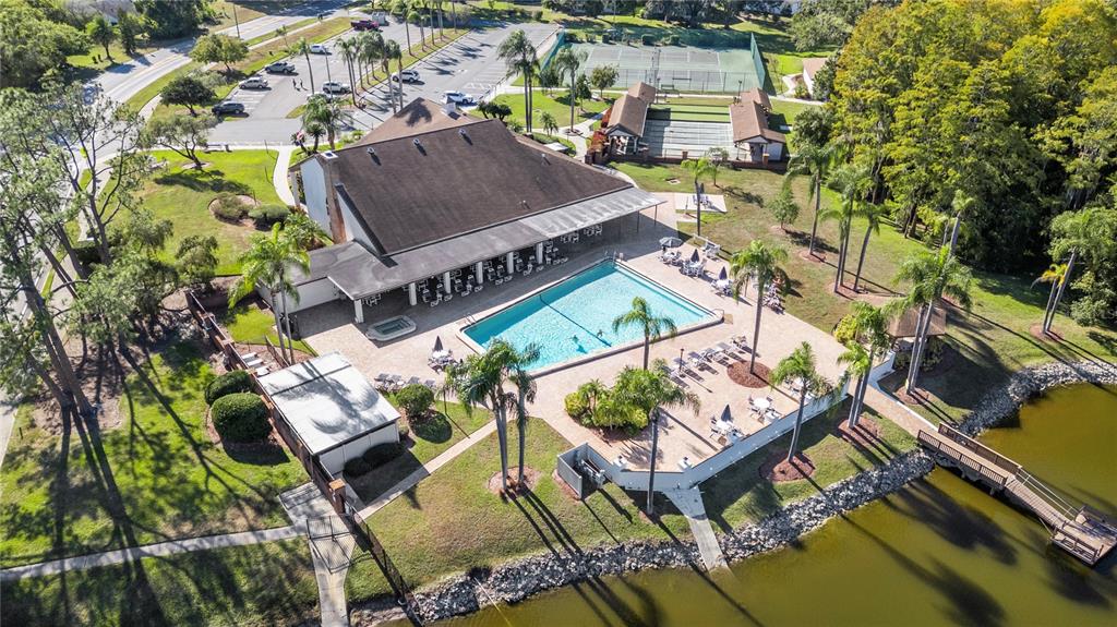 An aerial view shows a clubhouse with a swimming pool, tennis courts, and a lake — 9309 TROWBRIDGE COURT, NEW PORT RICHEY, FL