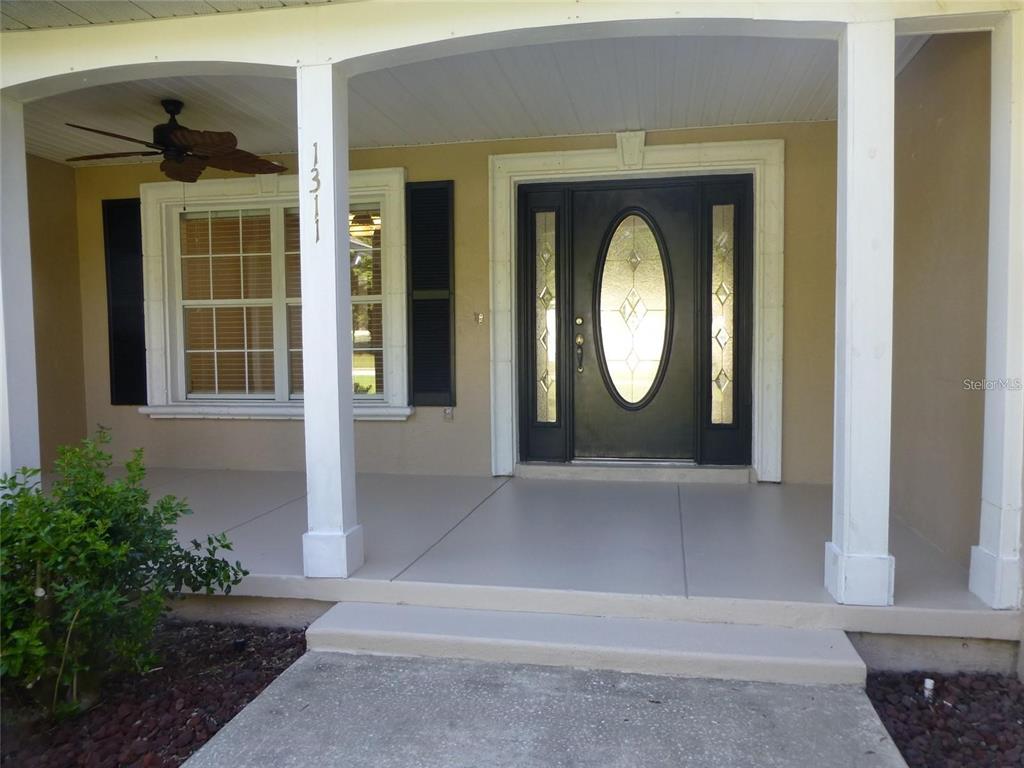 The front exterior of a house features a covered porch, a ceiling fan, and a door — 1311 SE 39TH COURT, OCALA, FL