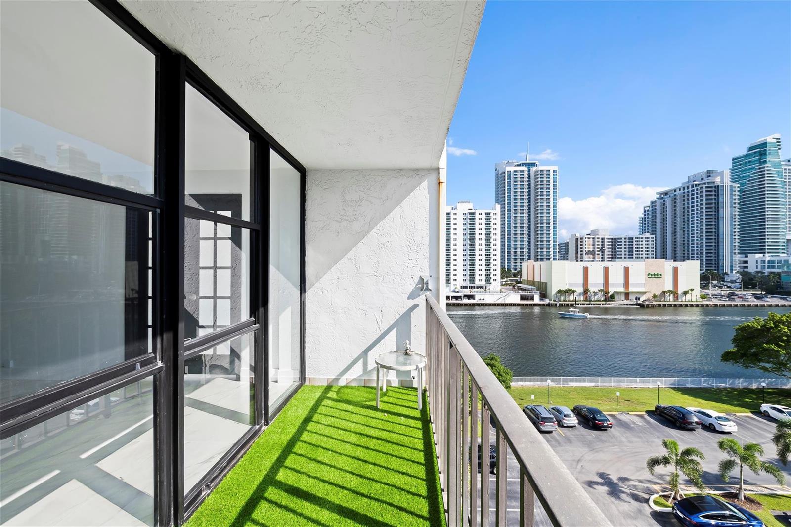 A balcony with artificial turf flooring overlooks a river, parking lot, and city skyline — 800 Parkview Drive # 718, Hallandale Beach FL 33009, HALLANDALE BEACH, FL