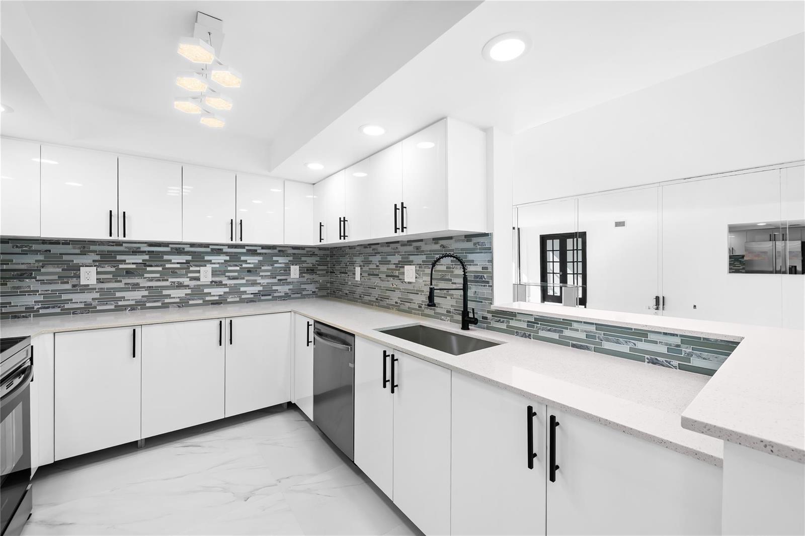 A modern kitchen features white cabinets, a gray tiled backsplash, and white countertops — 800 Parkview Drive # 718, Hallandale Beach FL 33009, HALLANDALE BEACH, FL