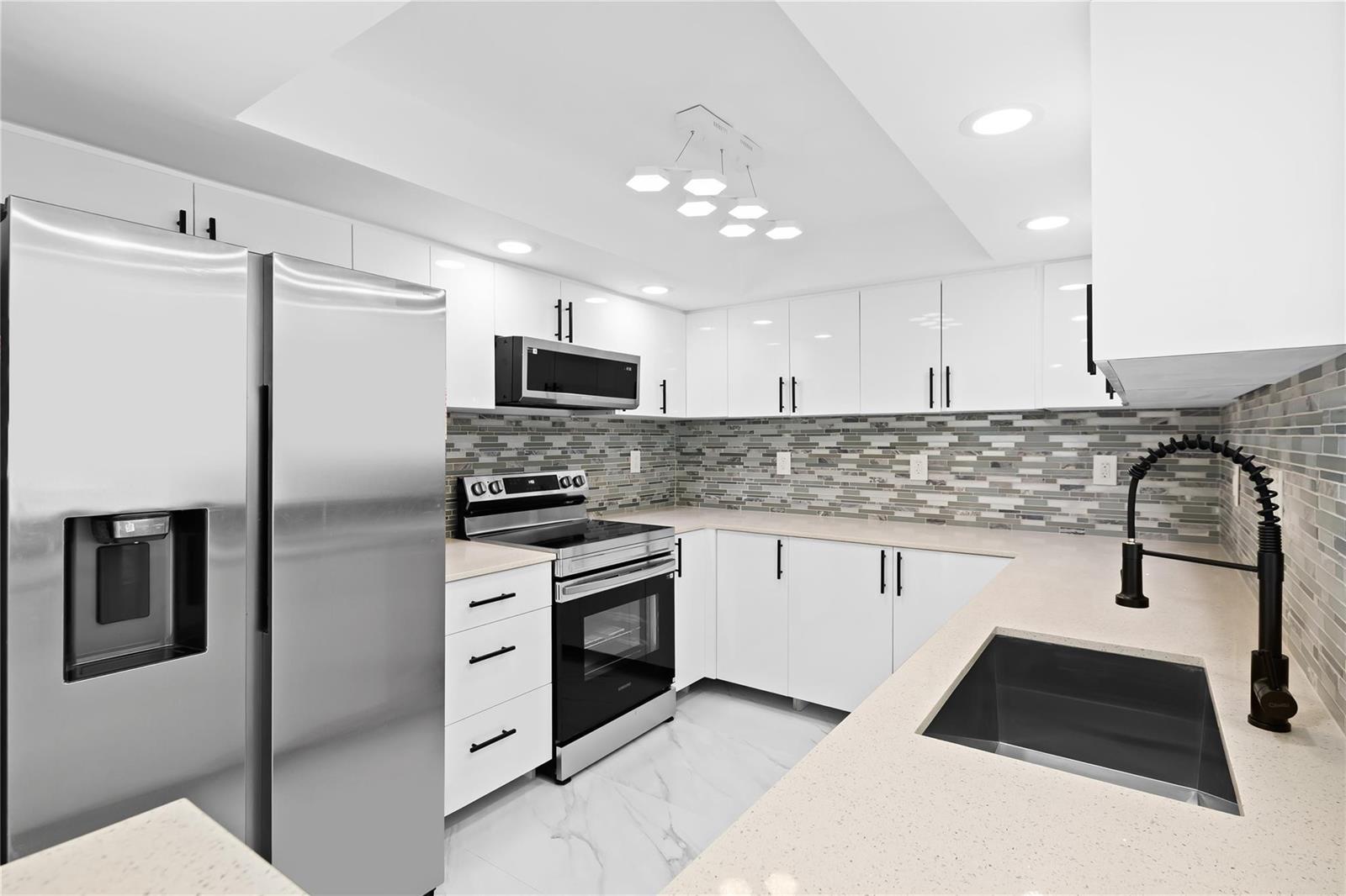 A modern kitchen features white cabinets, stainless steel appliances, a tiled backsplash, and quartz countertops — 800 Parkview Drive # 718, Hallandale Beach FL 33009, HALLANDALE BEACH, FL