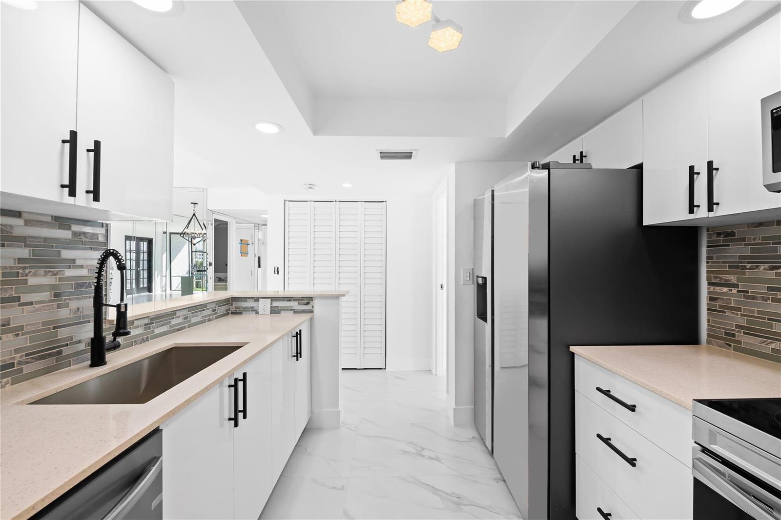 A modern kitchen features white cabinets, stainless steel appliances, quartz countertops, and a tiled backsplash — 800 Parkview Drive # 718, Hallandale Beach FL 33009, HALLANDALE BEACH, FL