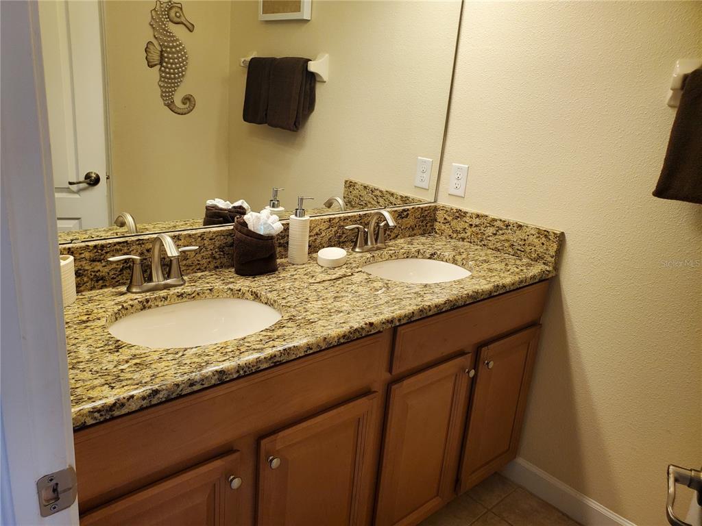 A bathroom features a double vanity with a granite countertop and wooden cabinets — 8965 CAT PALM ROAD, KISSIMMEE, FL