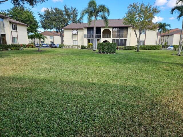 A large grassy lawn sits in front of two-story apartment buildings with palm trees — 105 Lake Pine Circle # 2, FL 33463, FL
