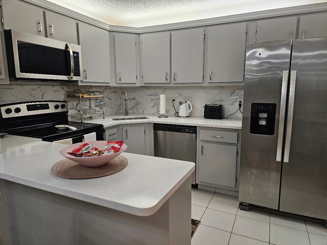 A kitchen features gray cabinets, stainless steel appliances, white countertops, and a marble-patterned backsplash — 105 Lake Pine Circle # 2, FL 33463, FL