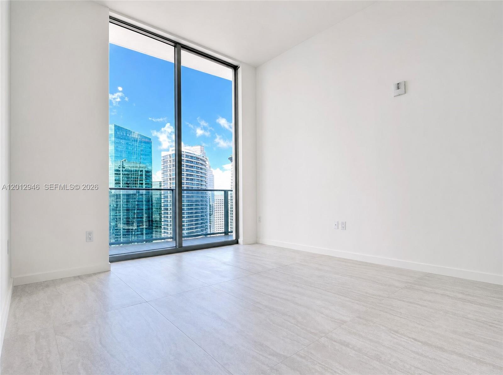 A bright, minimalist room features large floor-to-ceiling windows with a city skyline view — 77 SE 5 ST, Miami FL 33131, MIAMI, FL