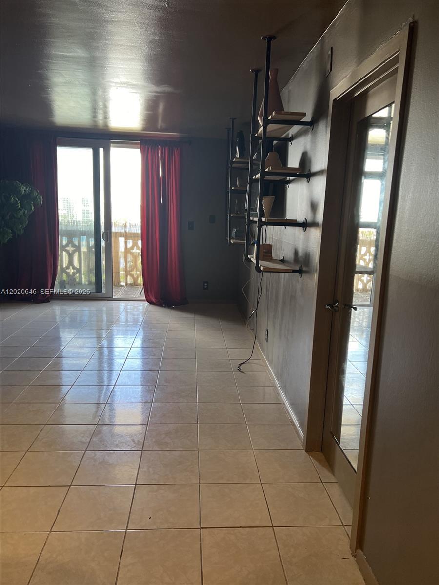 A room with tiled floors, red curtains, and industrial-style wall shelving leads to a balcony — 1817 S Ocean Dr # 718, Hallandale Beach FL 33009, HALLANDALE BEACH, FL