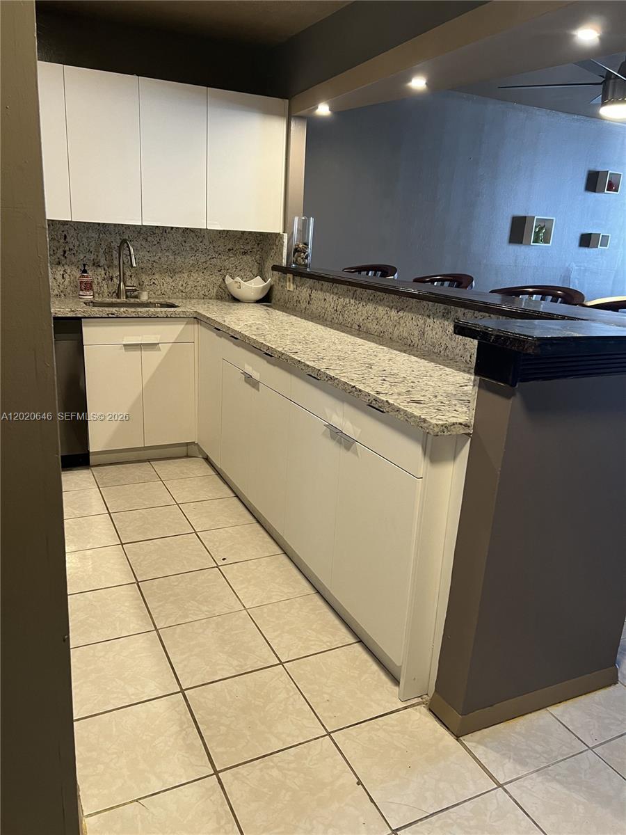 A kitchen features white cabinets, granite countertops, and a breakfast bar overlooking a living area — 1817 S Ocean Dr # 718, Hallandale Beach FL 33009, HALLANDALE BEACH, FL