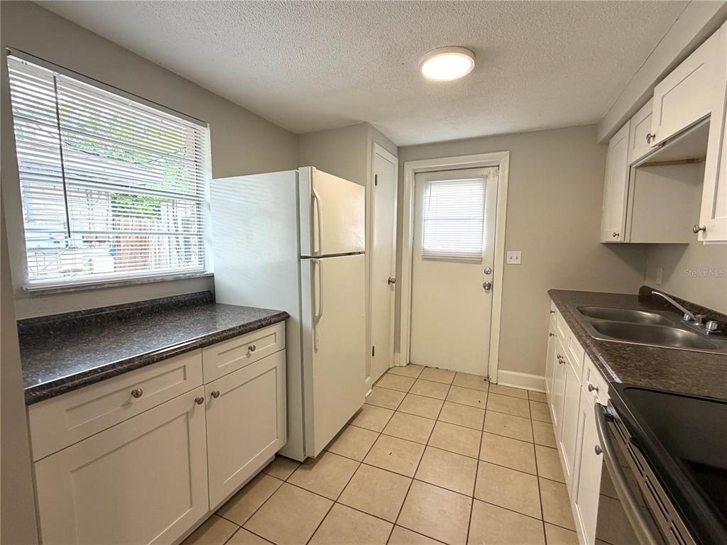A kitchen features white cabinets, dark countertops, a white refrigerator, and light-colored floor tiles — 10022 E WILDER AVENUE UNIT 12, TAMPA, FL