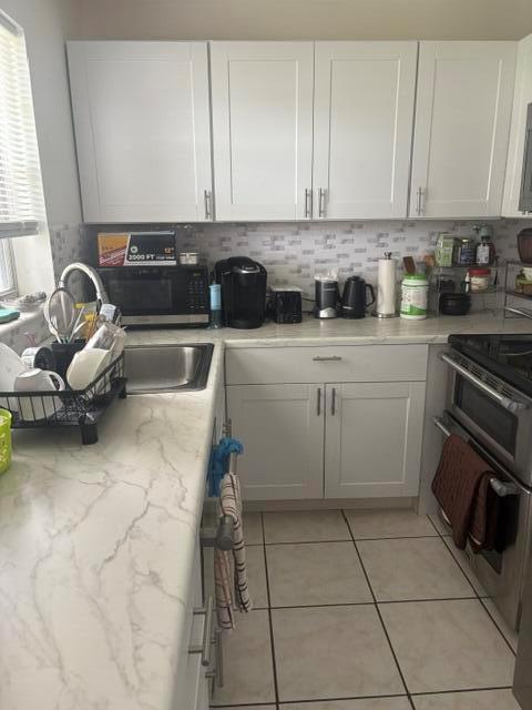 A kitchen features white cabinets, marble-patterned countertops, a stainless steel sink, and tile flooring — 145 Northampton # H, West Palm Beach FL 33417, WEST PALM BEACH, FL