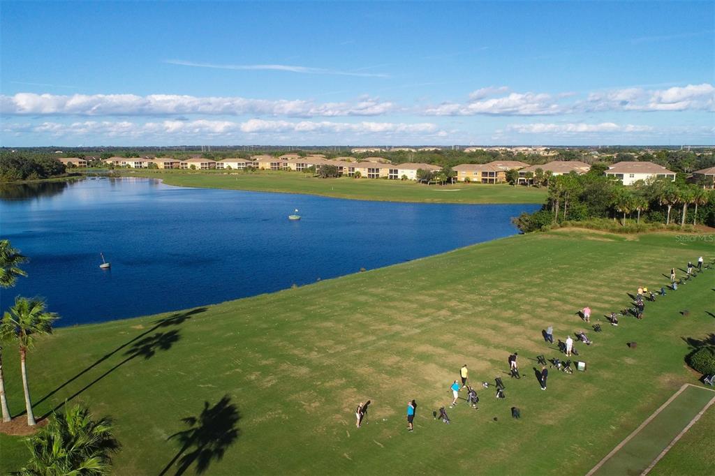 An aerial view of a golf driving range next to a lake and residential buildings — 7803 GRAND ESTUARY TRAIL UNIT 208, BRADENTON, FL